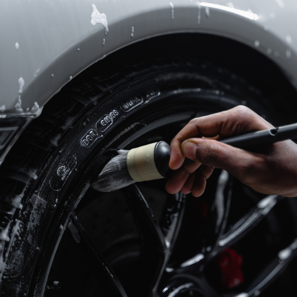 "A close-up of a car wheel being meticulously detailed with a brush by a professional, removing dirt and grime for a shiny finish.